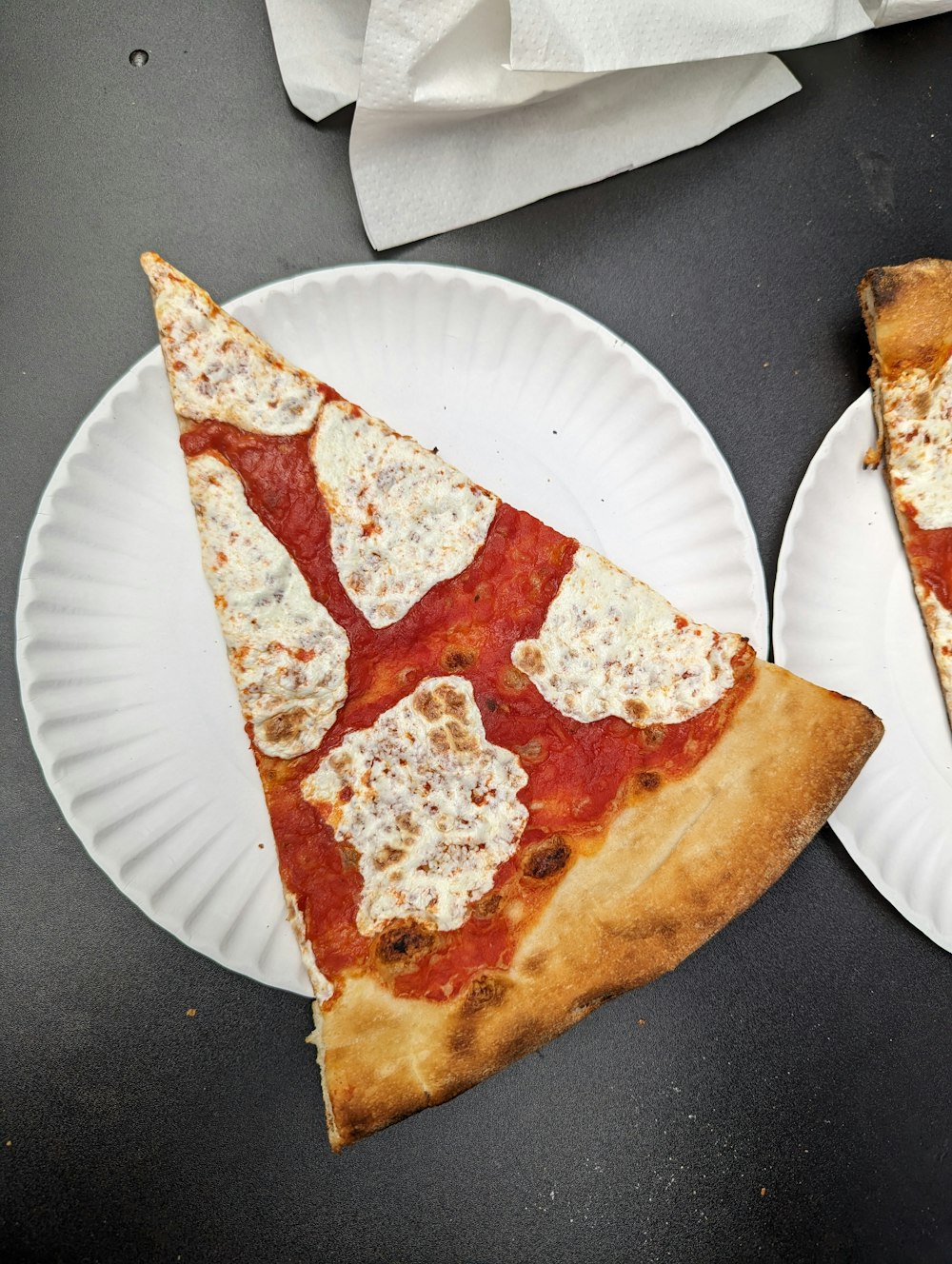 two slices of pizza on paper plates on a table