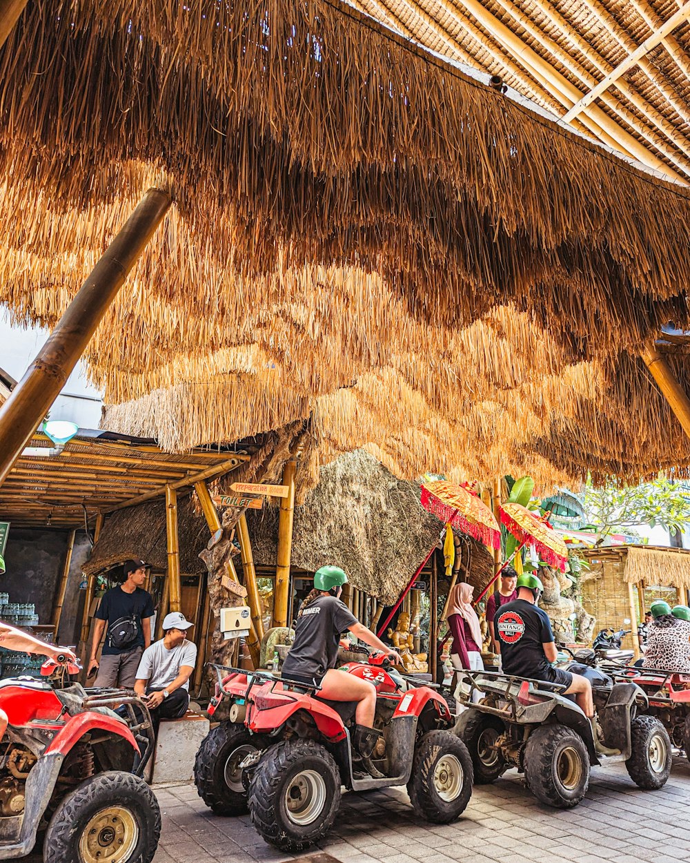 a group of people riding four wheelers under a thatched roof