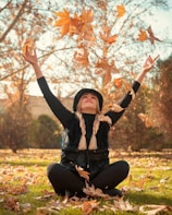 a woman is sitting on the grass throwing leaves in the air