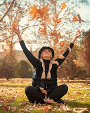 a woman is sitting on the grass throwing leaves in the air