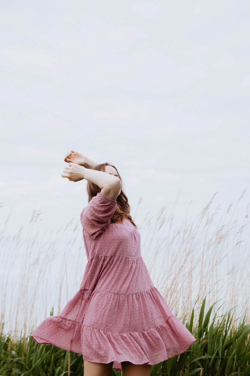 une femme dans une robe rose debout dans les hautes herbes
