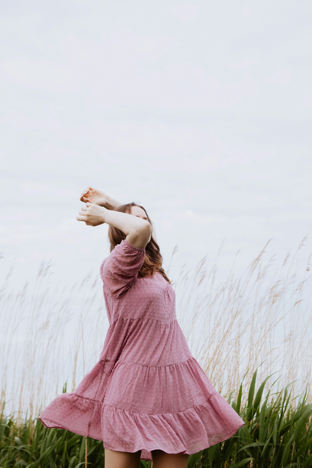 a woman in a pink dress standing in tall grass