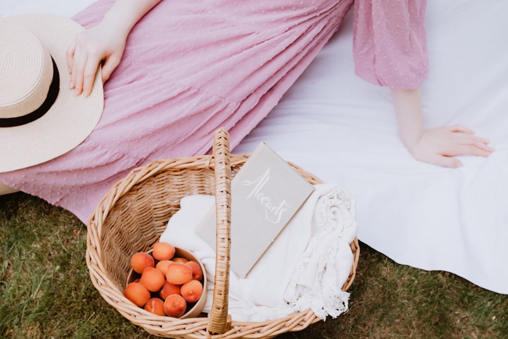 a woman in a pink dress sitting on the grass with a basket of oranges
