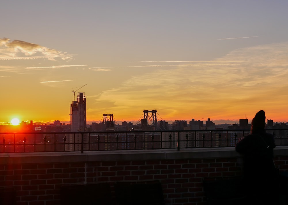 a person standing on a bridge watching the sun set