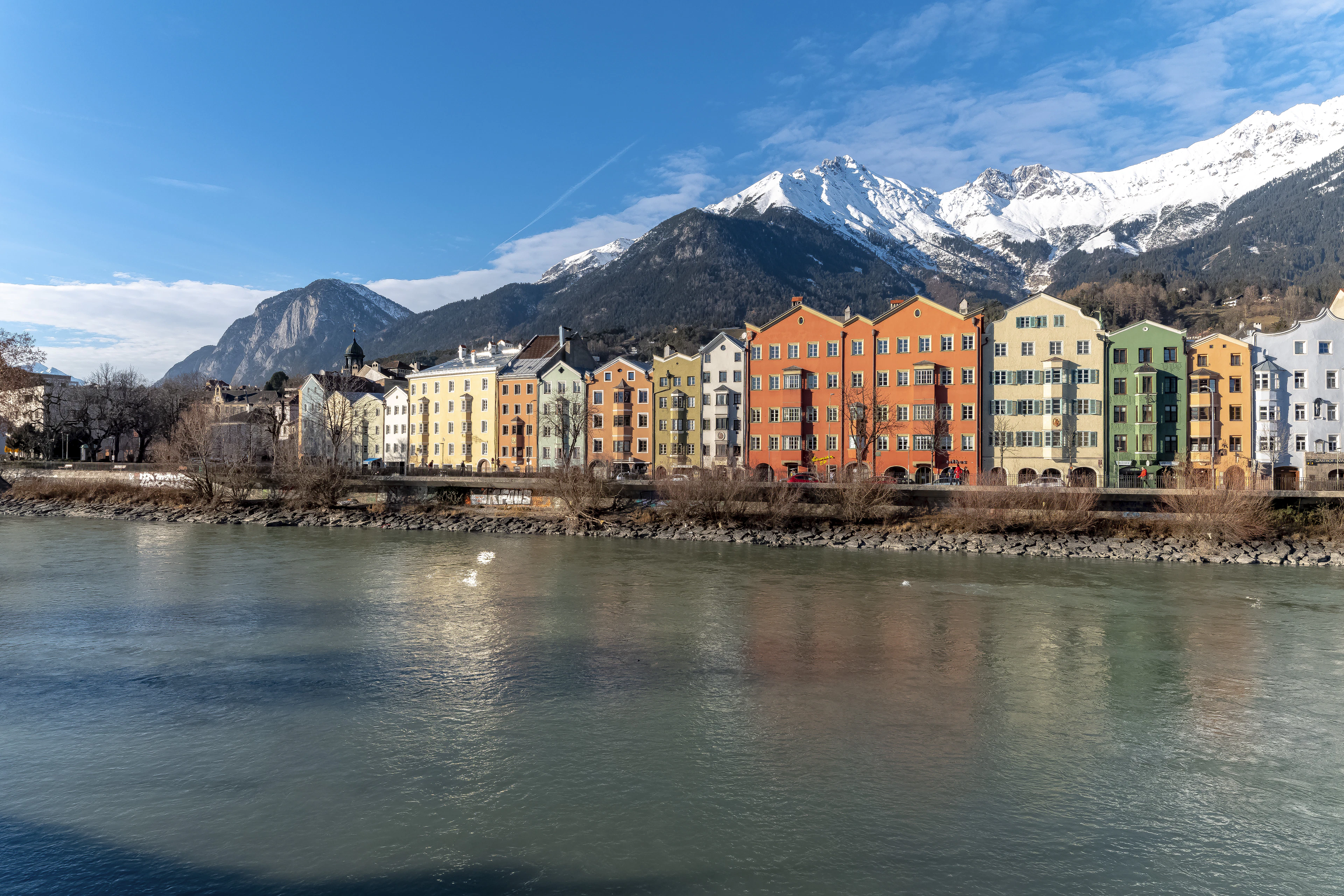 The pastel riverside houses of Innsbruck reflected in the Inn river, with the snow-covered Nordkette range towering behind