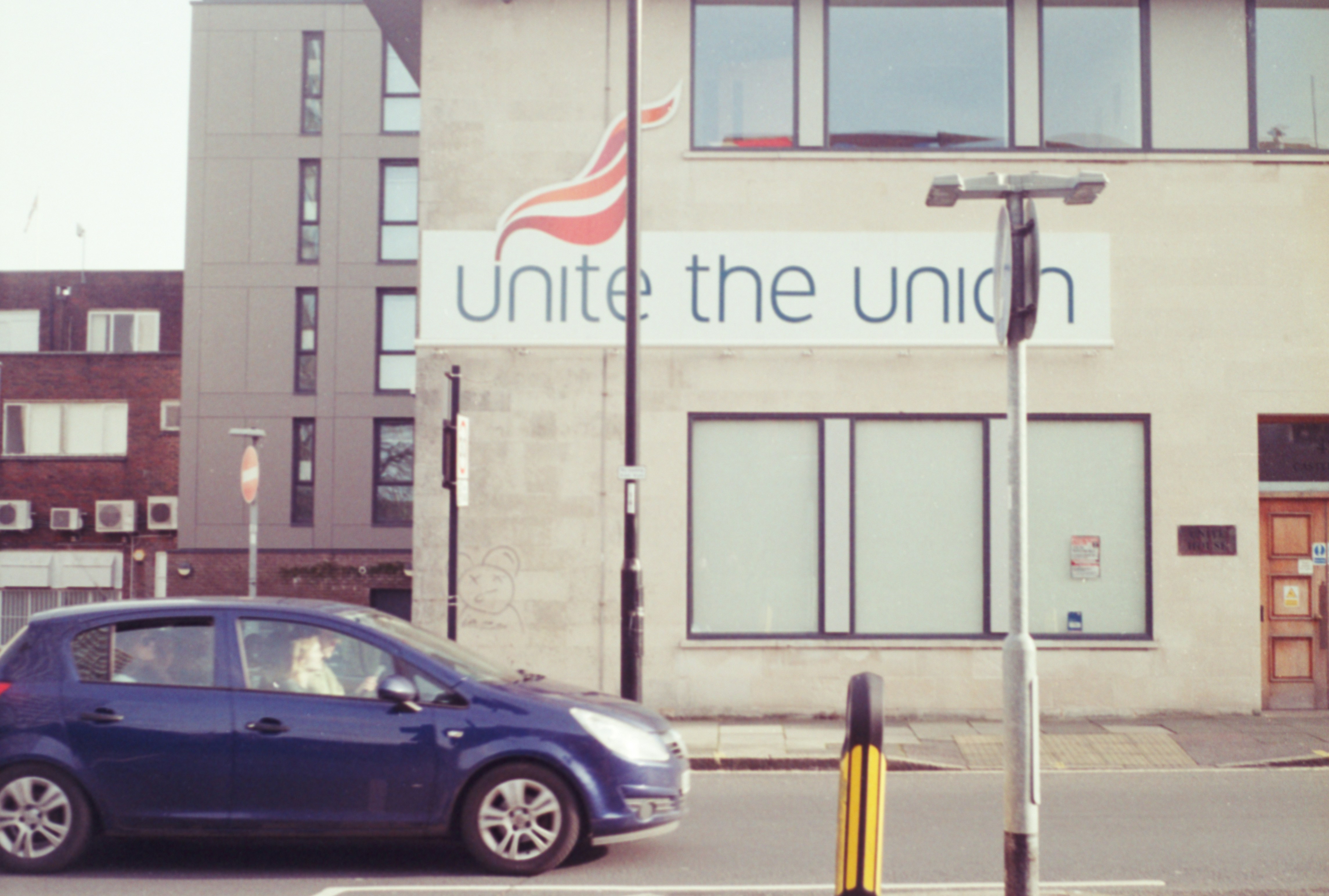 a small blue car driving past a tall building