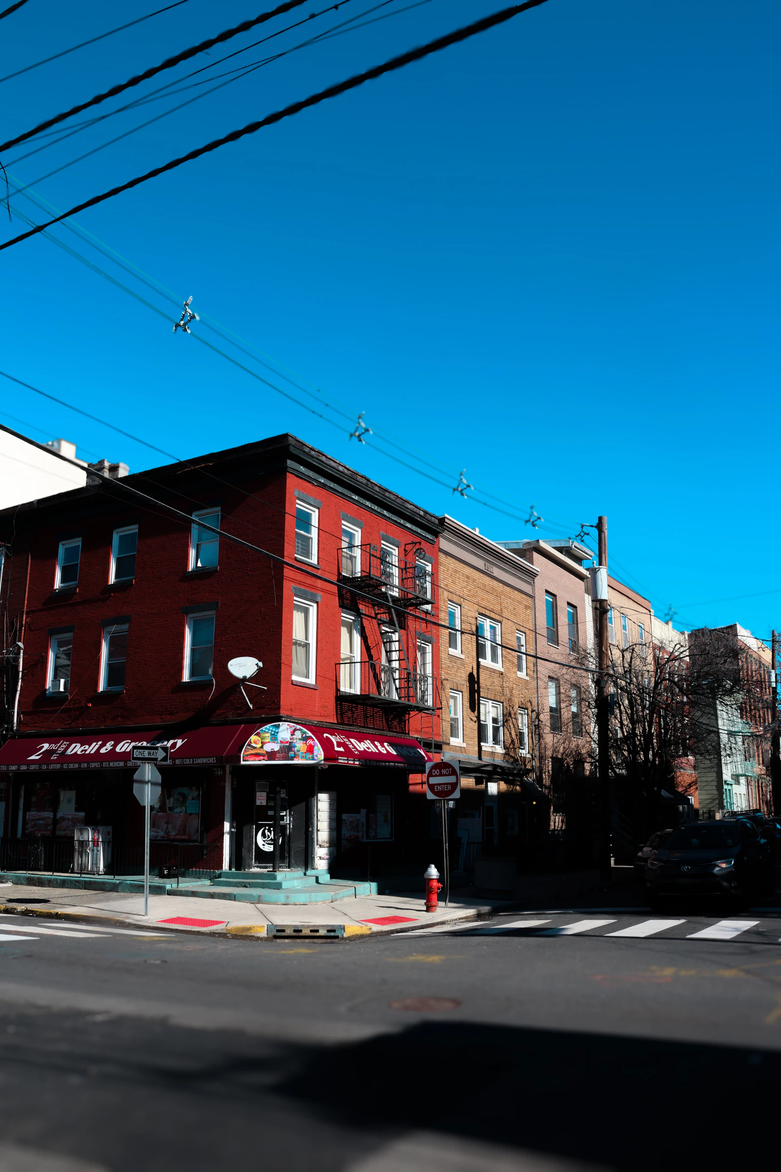 Travel photograph: A red-brick corner deli and low residential buildings beneath a vivid blue sky in Jersey City.