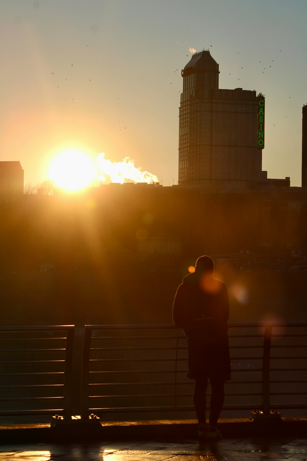 a person standing on a bridge with the sun setting in the background