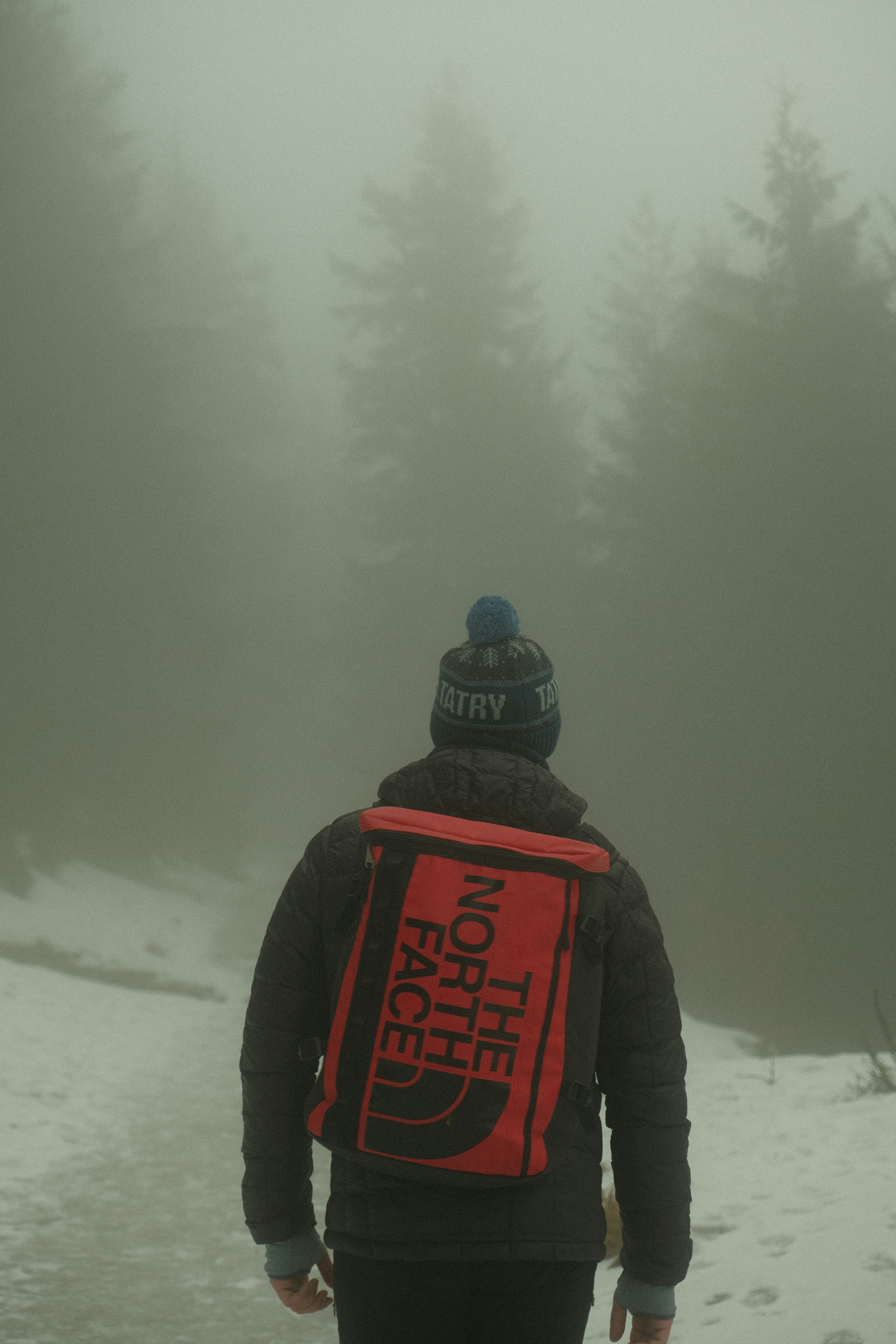 a man with a red backpack walking in the snow