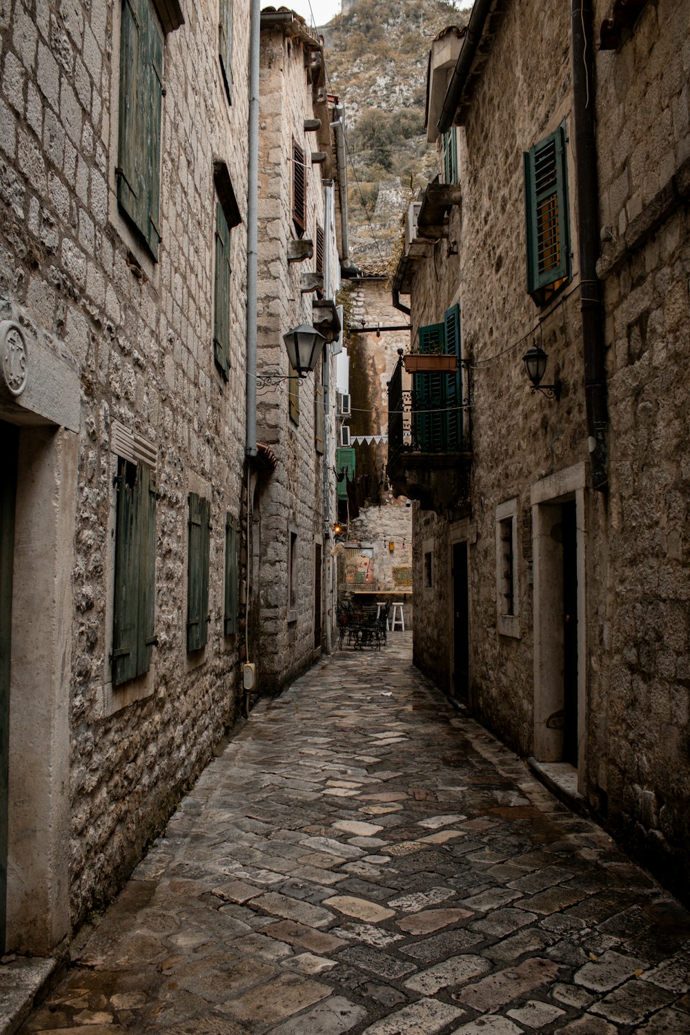 a cobblestone street with stone buildings and green shutters