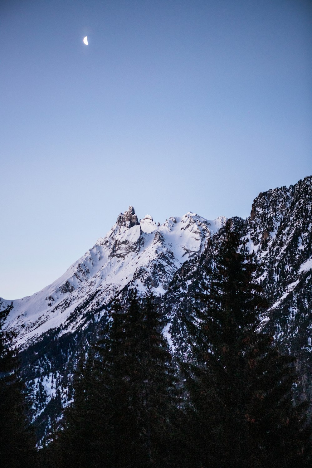 a snow covered mountain with a half moon in the sky