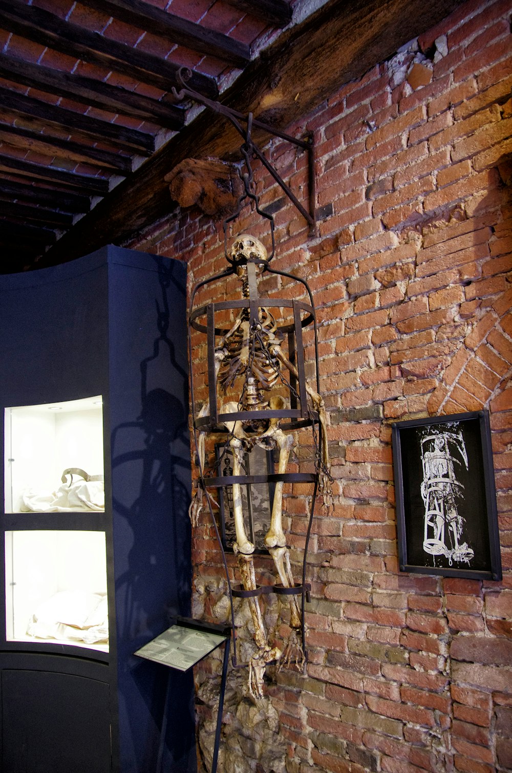 a skeleton in a cage hanging on a brick wall