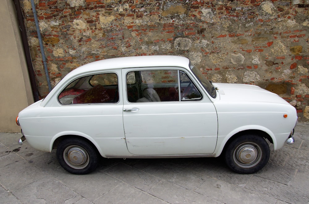 a small white car parked in front of a brick wall