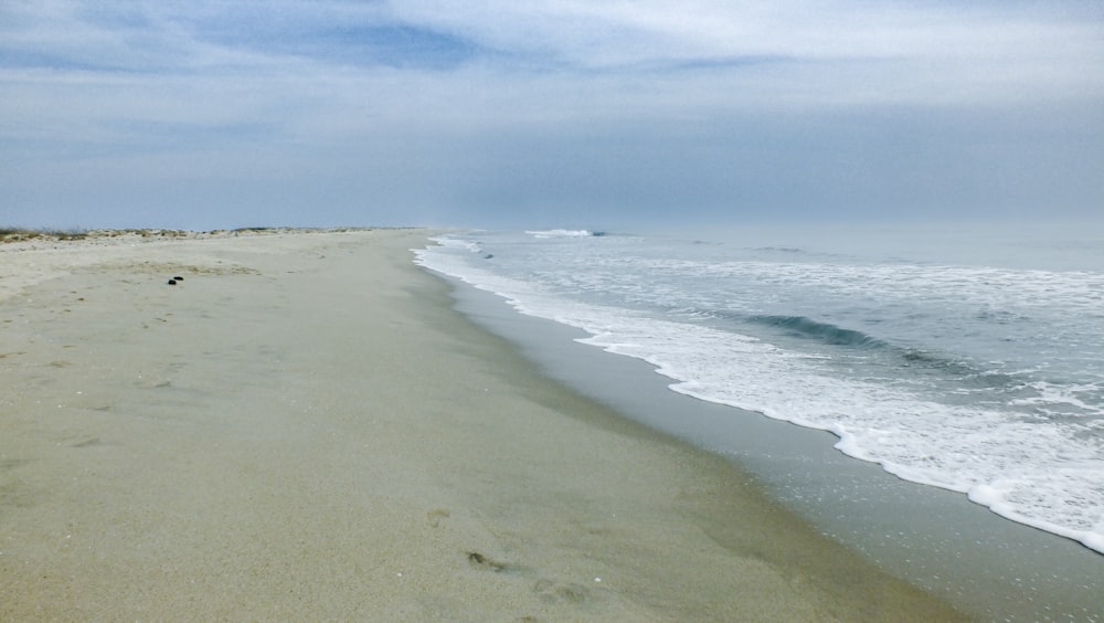 a sandy beach next to the ocean under a cloudy sky