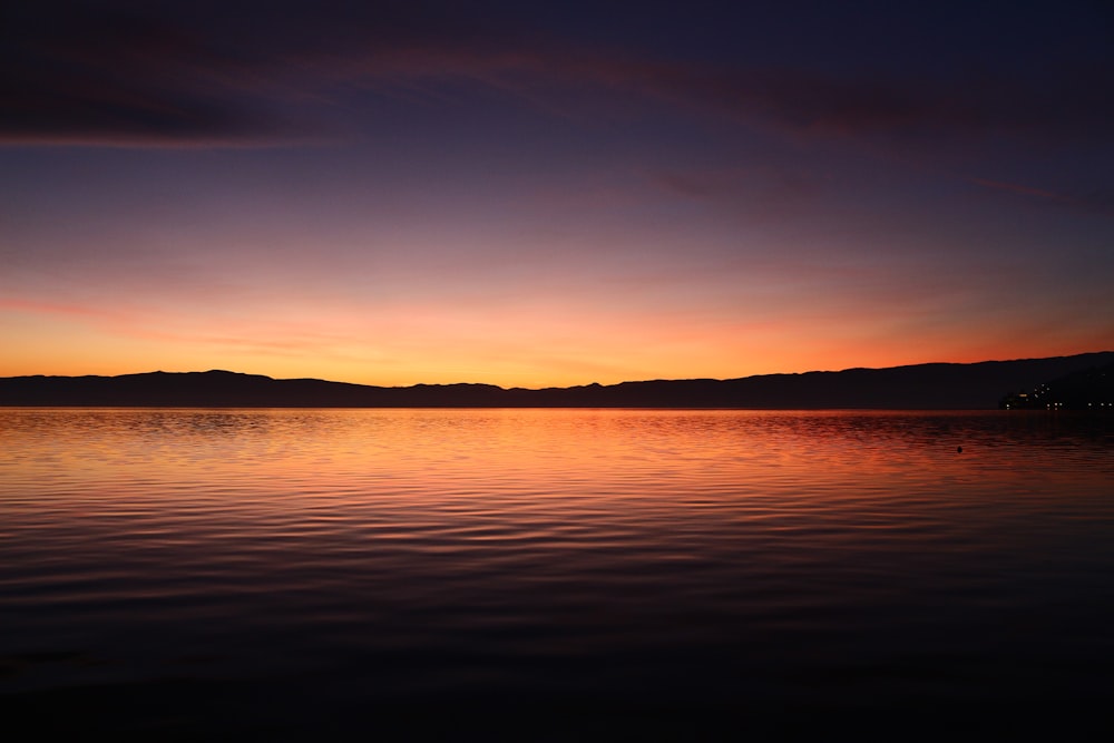 a sunset over a body of water with mountains in the background