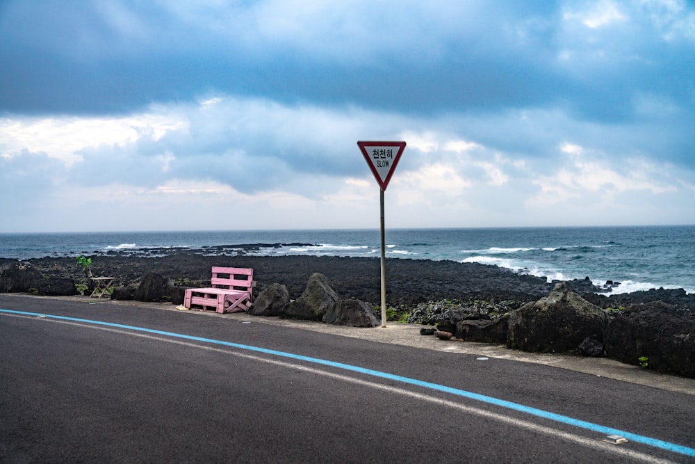 a pink bench sitting on the side of a road next to the ocean