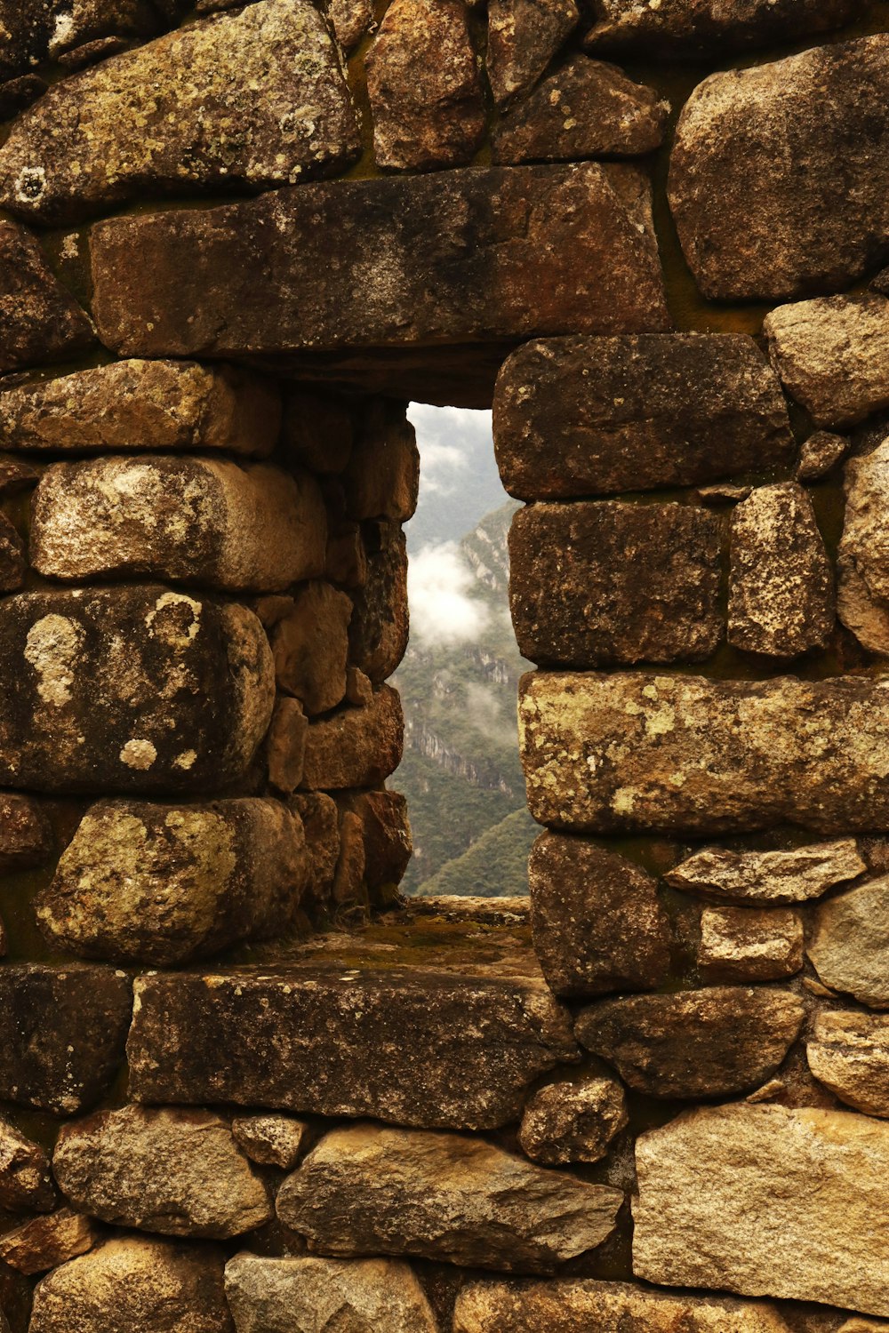 a window in a stone wall with a mountain in the background
