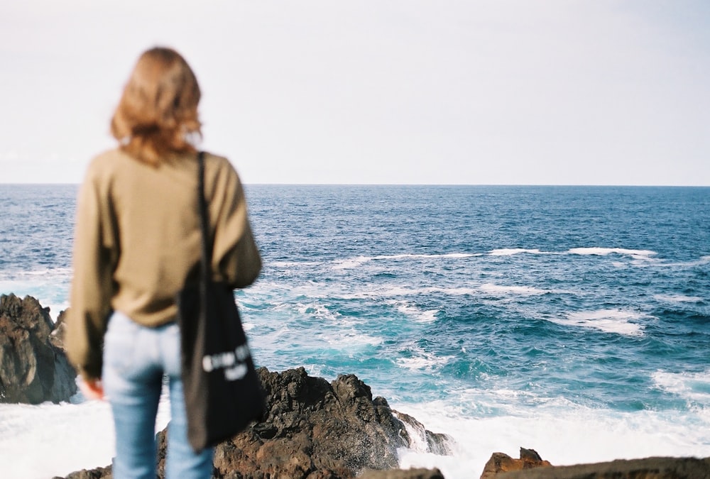 eine Frau, die auf einem Felsen steht und auf das Meer blickt