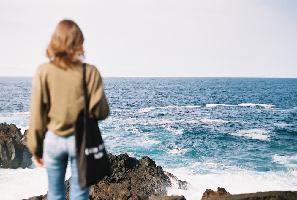 uma mulher em pé em uma rocha olhando para o oceano