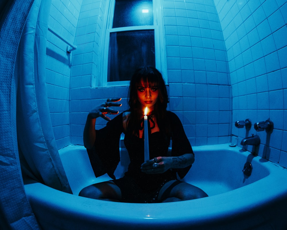 a woman sitting in a bathtub holding a candle