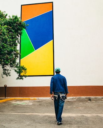 a man walking down a street past a large painting