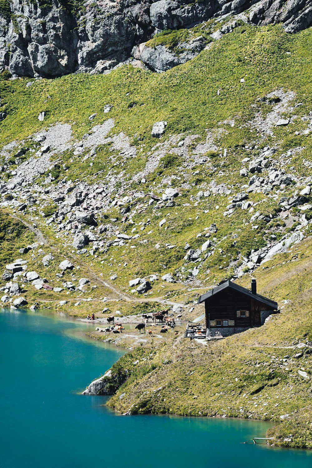 a small cabin on the side of a mountain next to a lake