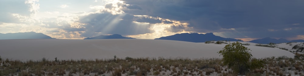 the sun shines through the clouds over the sand dunes