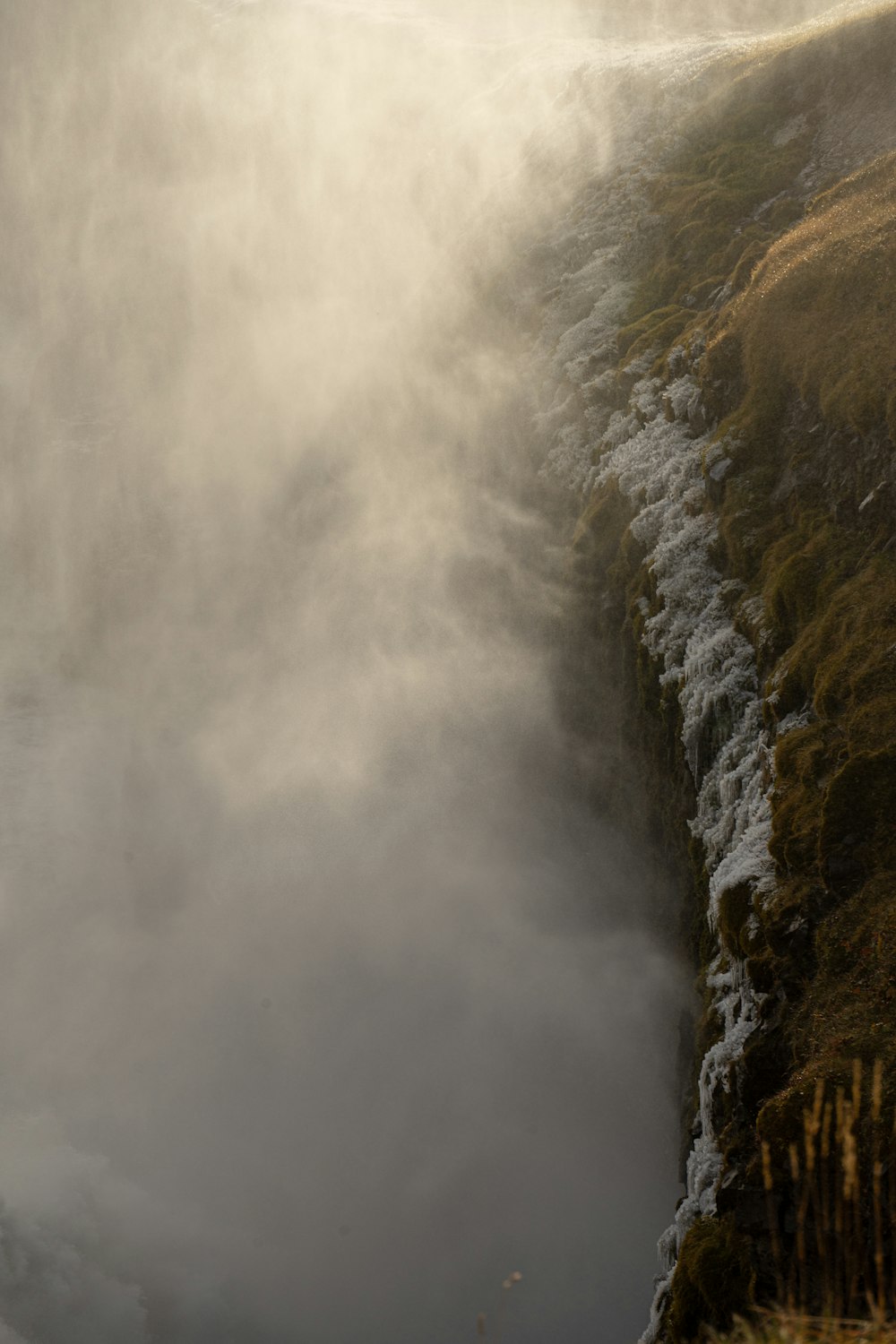 a foggy mountain side with a waterfall in the foreground