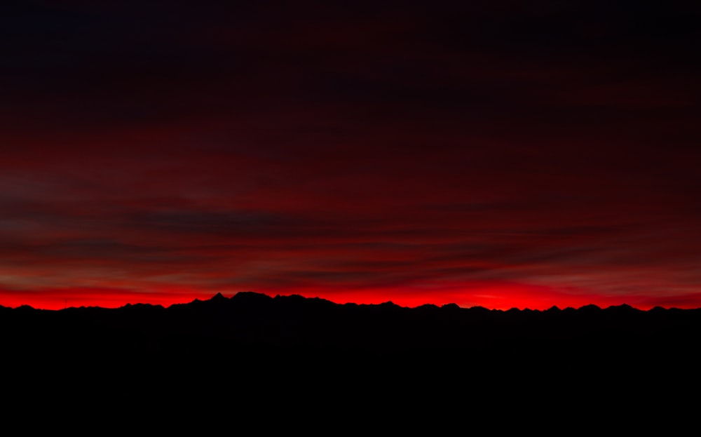 a red and black sky with a line of mountains in the distance