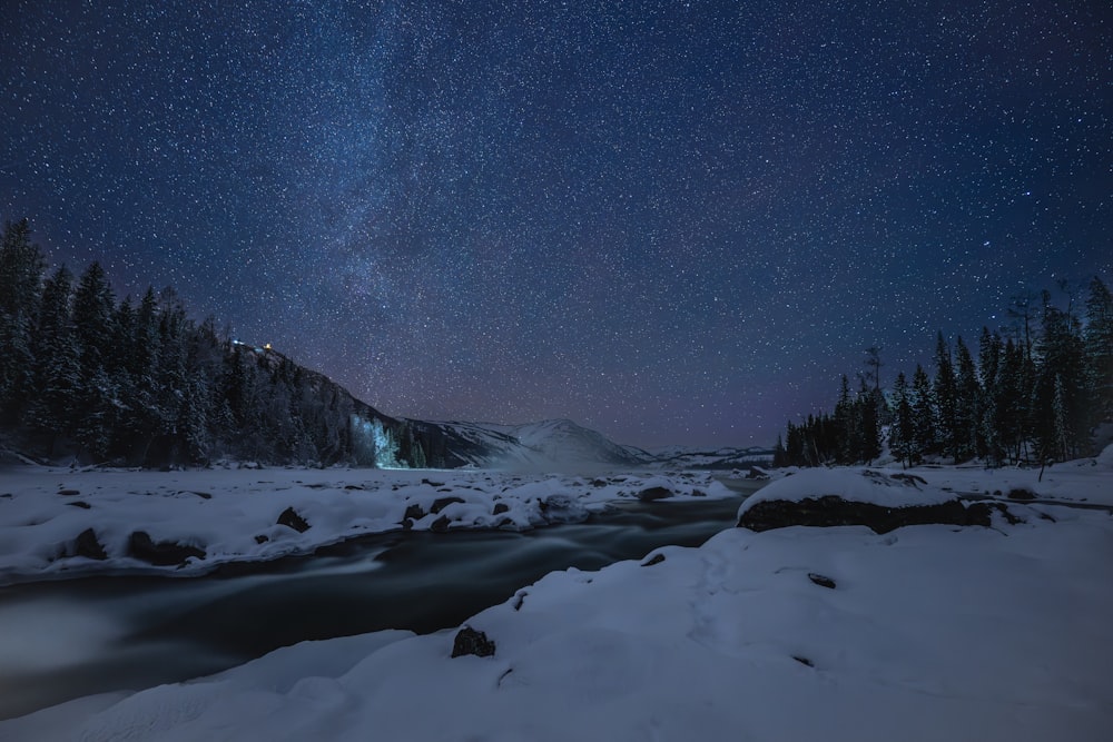 a river running through a snow covered forest under a night sky