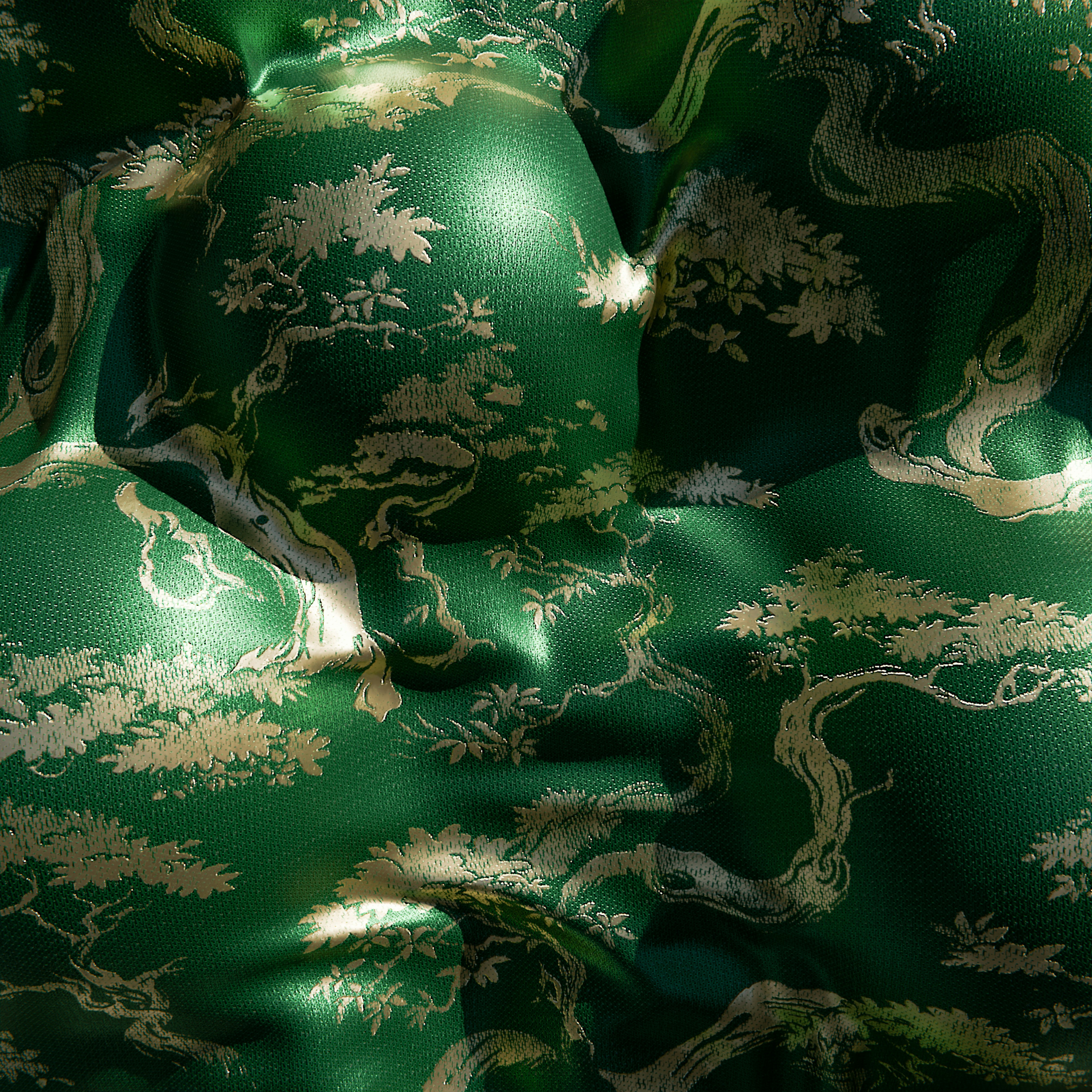 A close-up of a green fabric with a woven gold/tan pattern of trees and flowers.