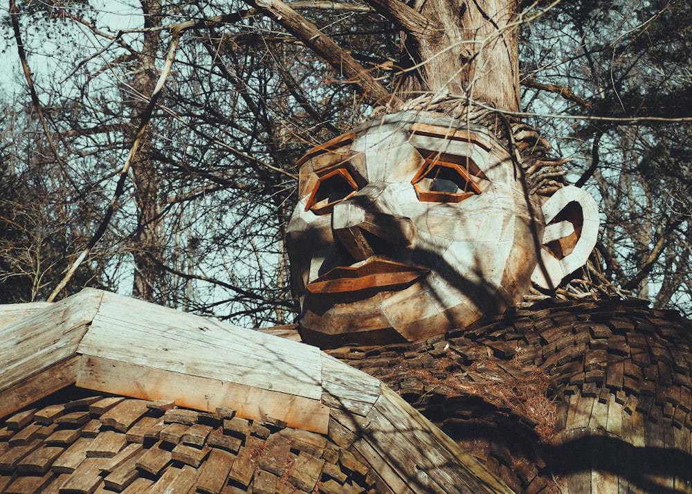 una máscara de madera sentada en lo alto de un techo junto a un árbol