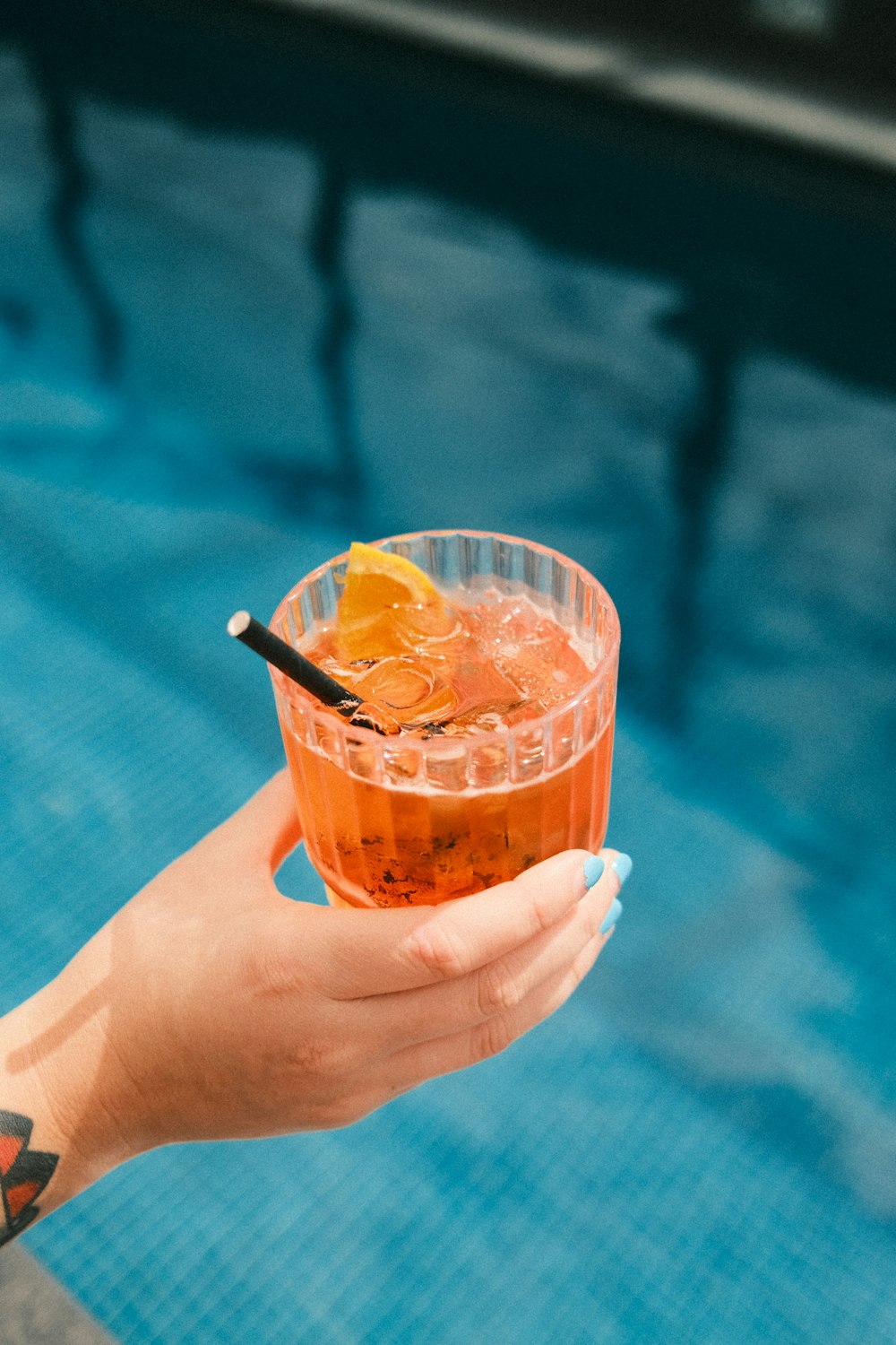 a person holding a drink near a swimming pool