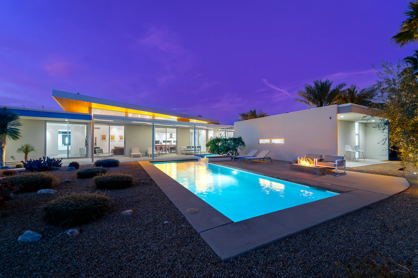 Modern home with a lit pool at twilight