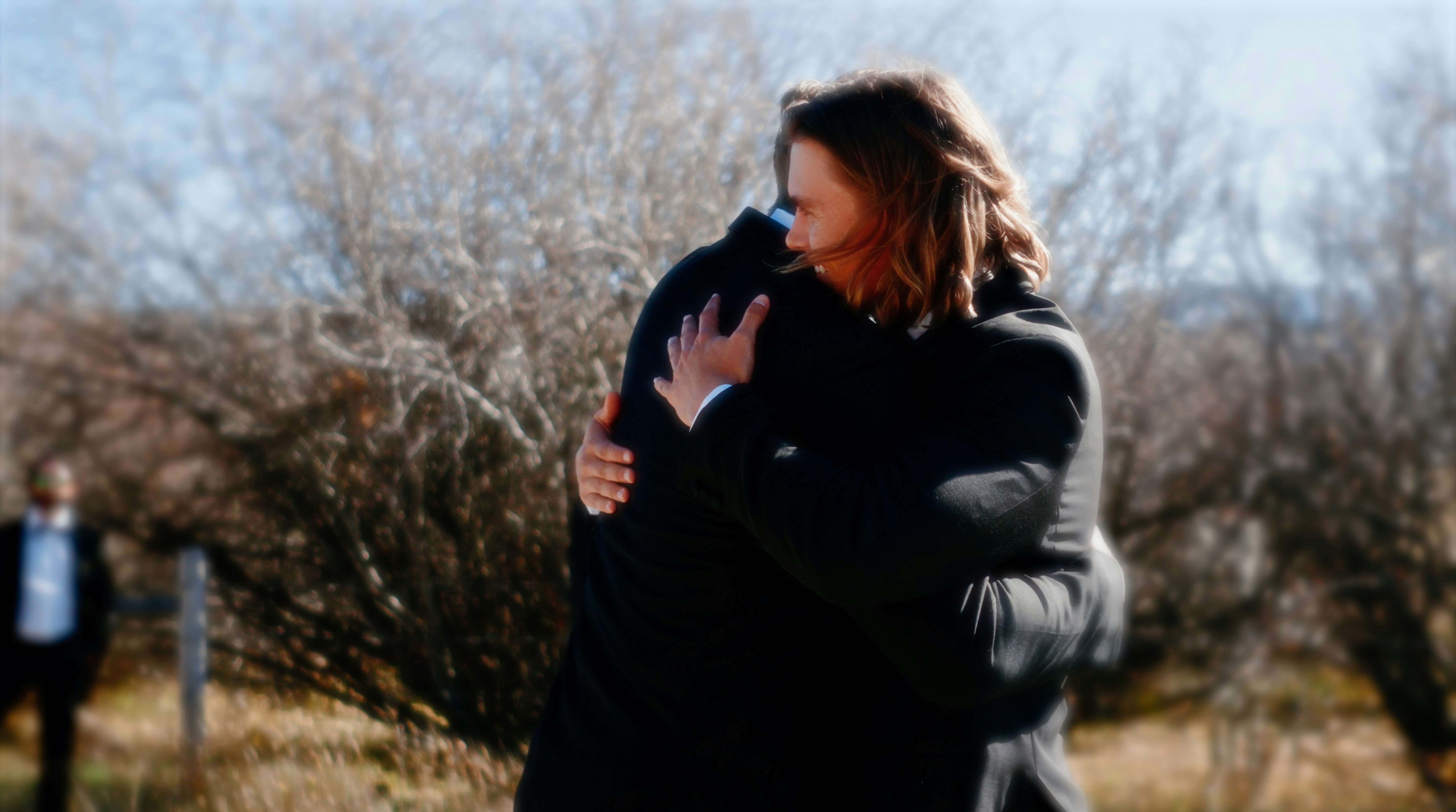 A somber photo of a grieving family member, with blurred faces in the background, possibly indicating a memorial or aftermath