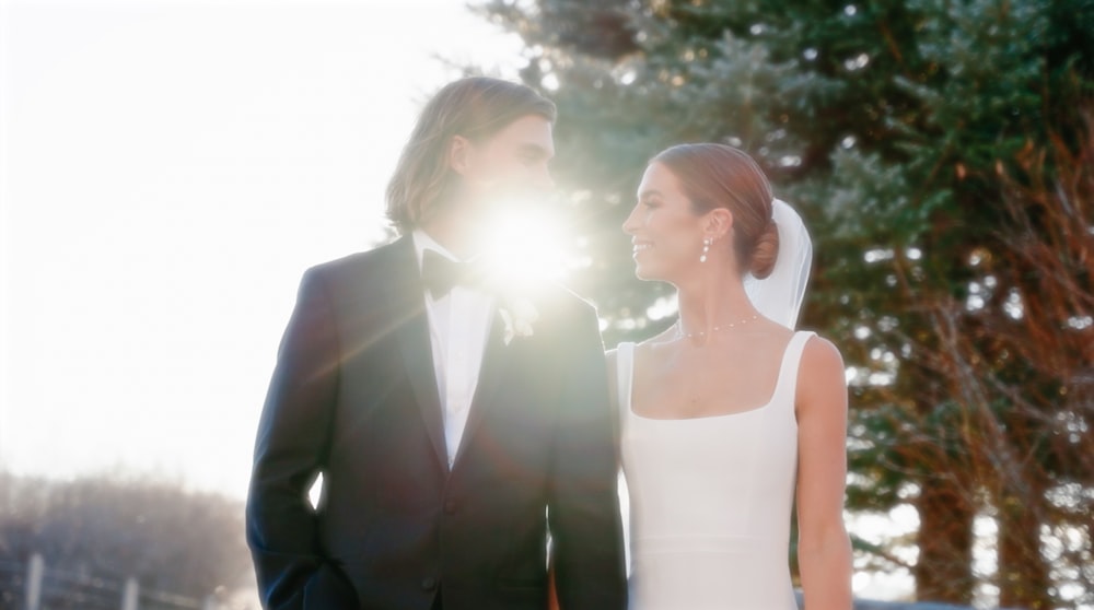 a bride and groom standing together in front of trees