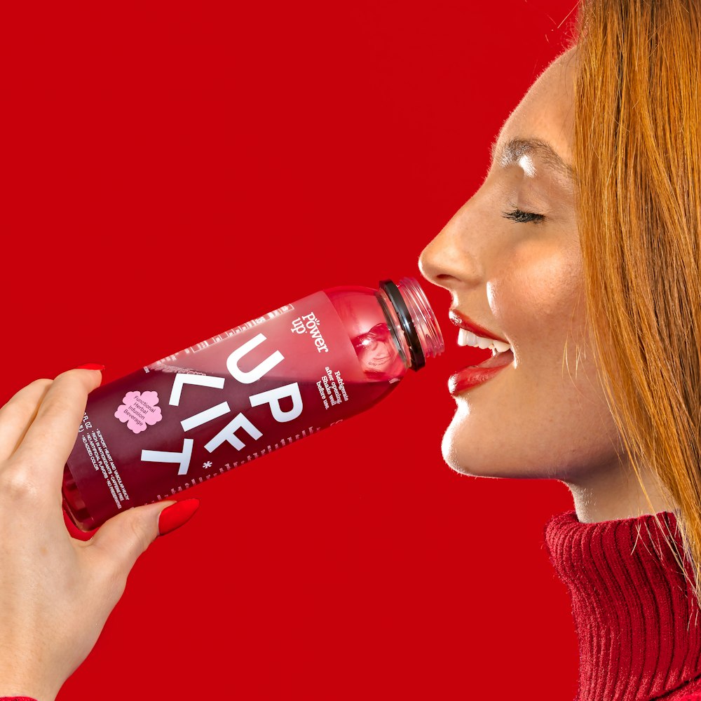a woman drinking a red drink from a bottle