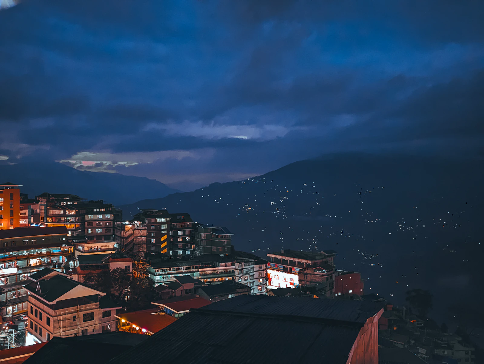 Gangtok at blue hour, lit apartment blocks in the foreground and house lights scattered across the dark ridges beyond