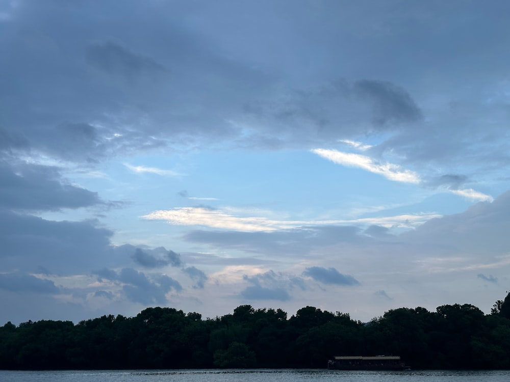 a body of water surrounded by trees under a cloudy sky