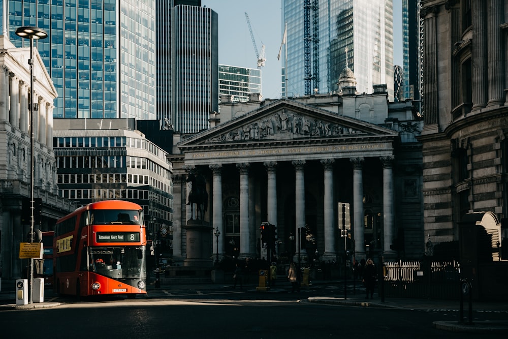 a red double decker bus driving down a street next to tall buildings