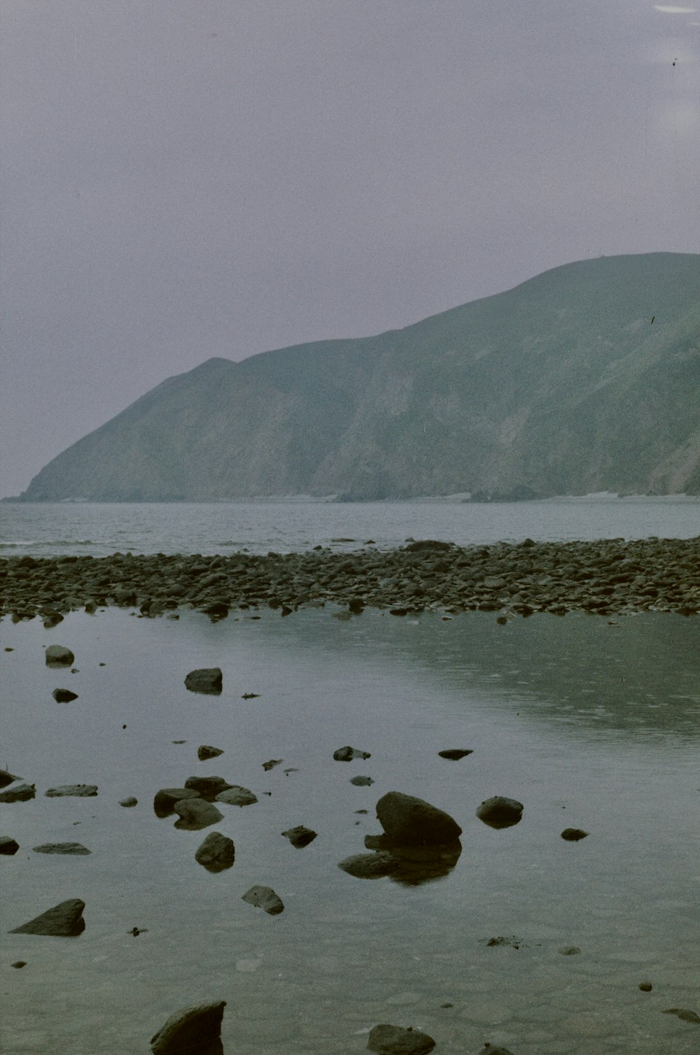 a beach with rocks in the water and a mountain in the background