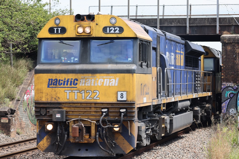 a yellow and blue train traveling under a bridge