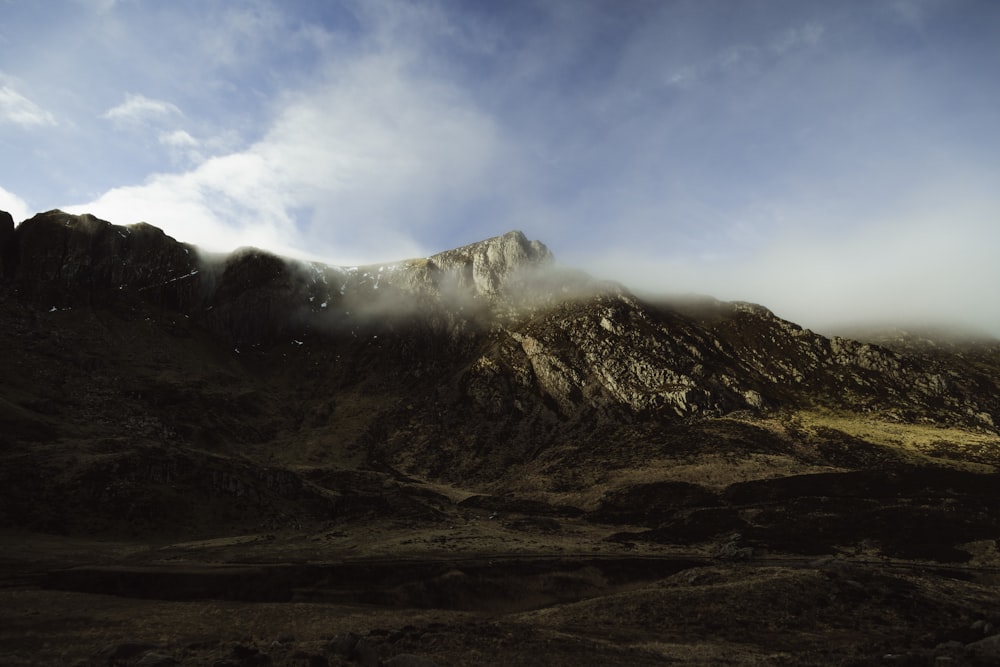 a mountain covered in fog and clouds under a blue sky