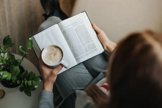 a woman reading a book while holding a cup of coffee