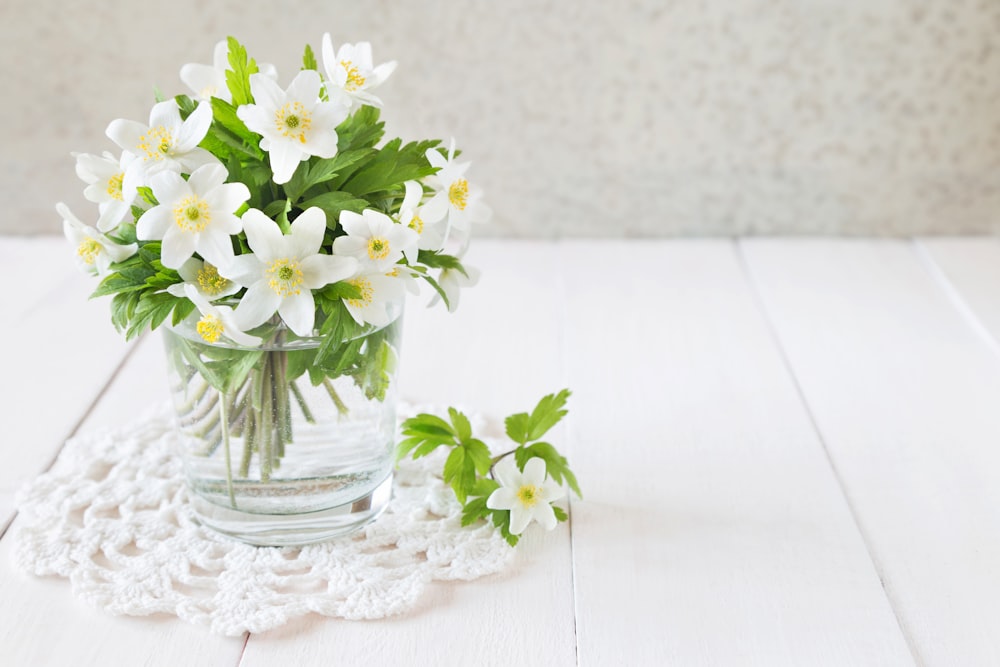 un jarrón de vidrio lleno de flores blancas encima de una mesa