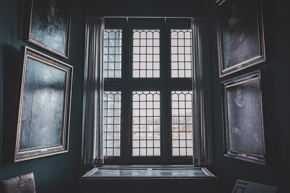 a window in a dark room with framed pictures on the wall