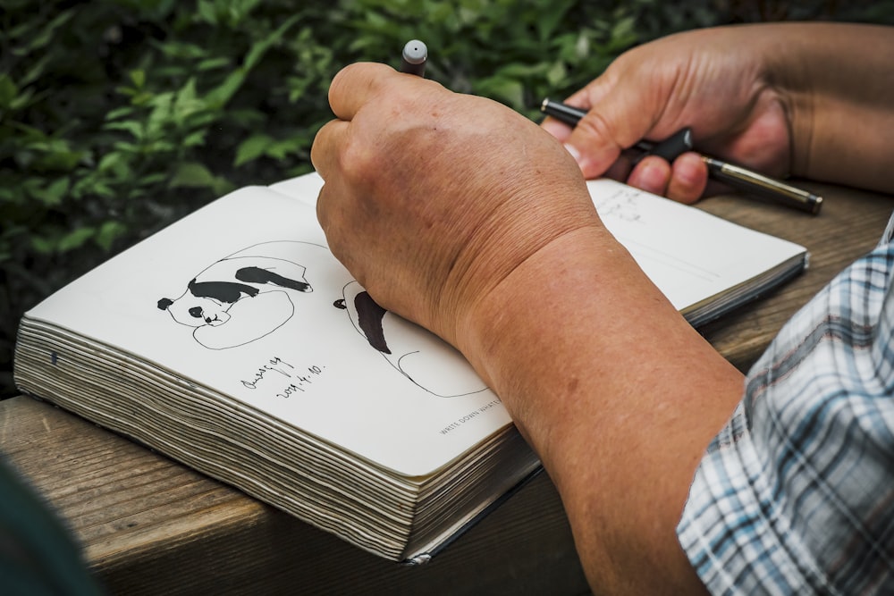 a person writing on a notebook with a pen