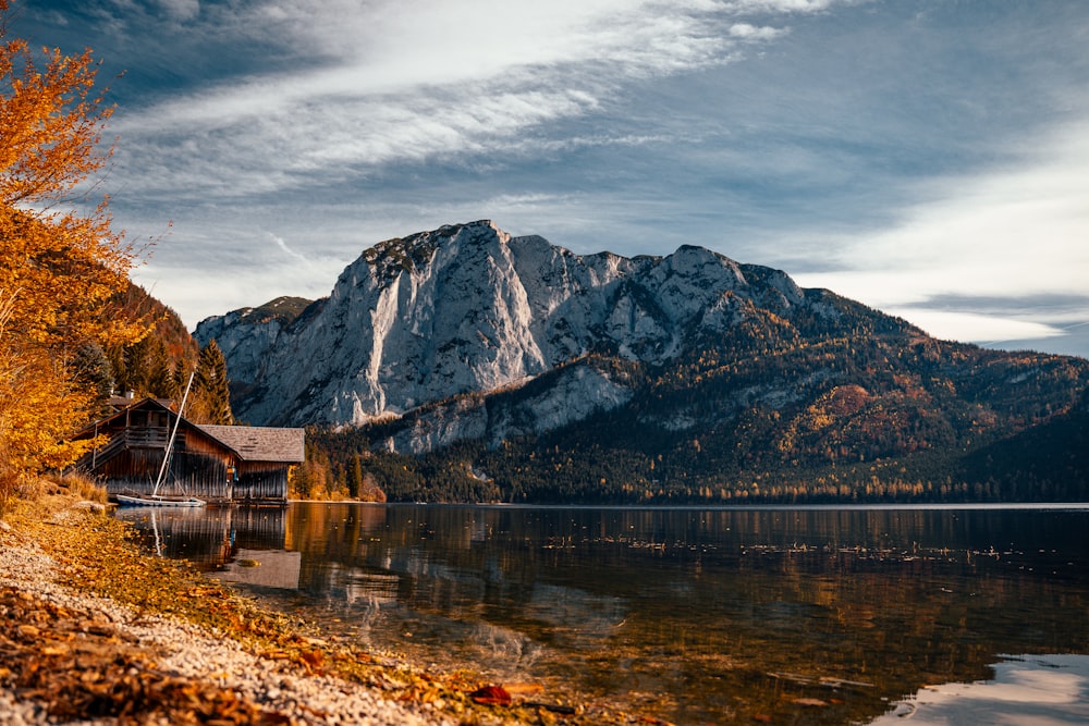 a cabin on the shore of a lake with mountains in the background
