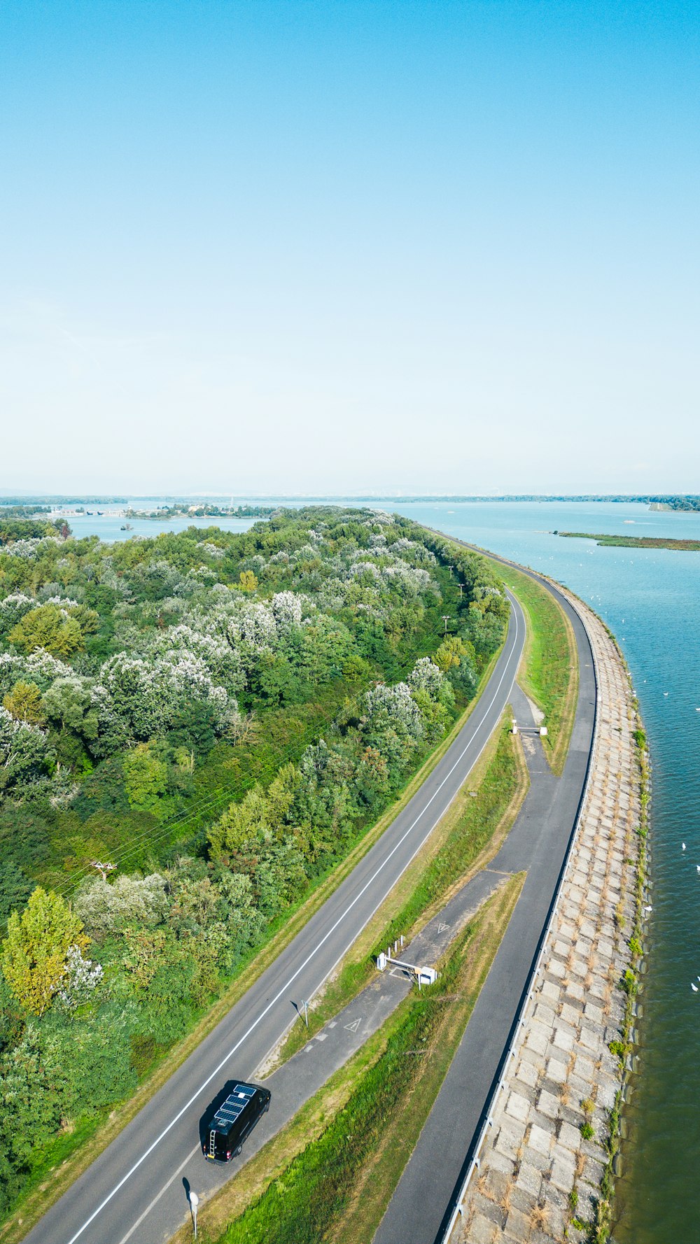 a black car driving down a road next to a body of water