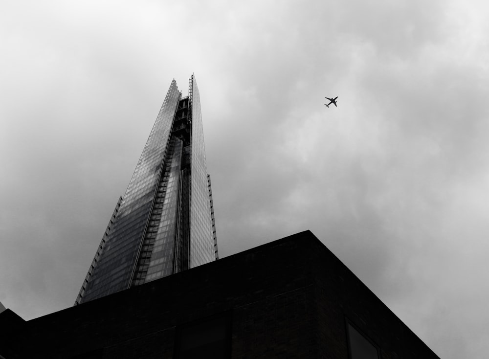 a plane flying over a tall building under a cloudy sky